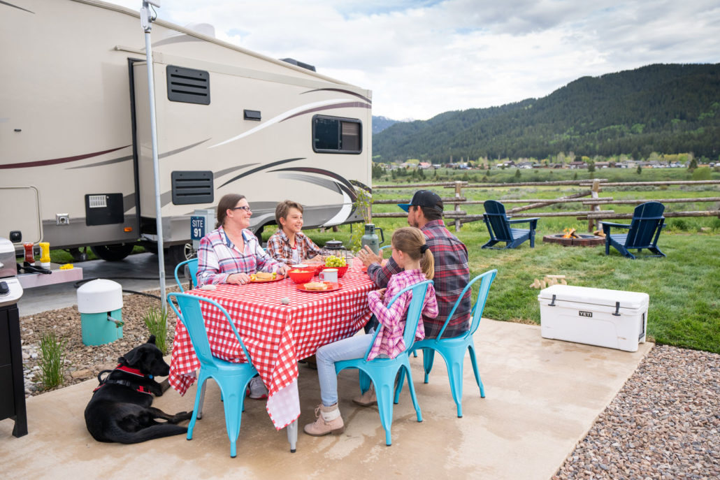 A family eating dinner at a red picnic table in front of their RV in Alpine, Wyoming.