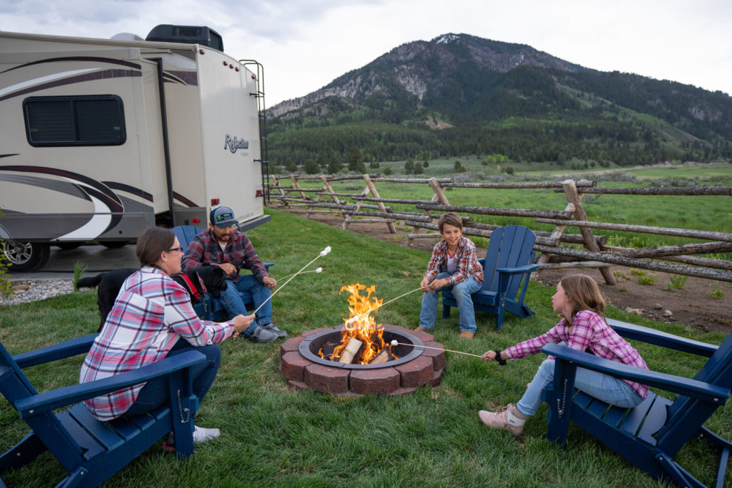 A family of four roasting marshmallows over a campfire next to their RV at Alpine Valley RV Resort.