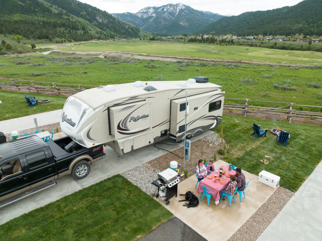 A family eating dinner at a red picnic table in front of their RV at a premium back-in campsite.