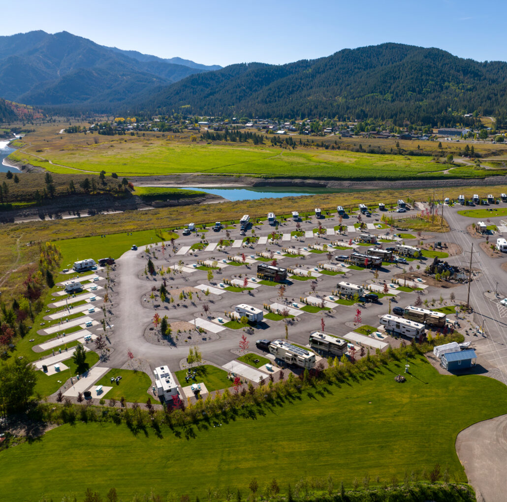 Birds eye view of an RV campground surrounded by green grass and mountains.