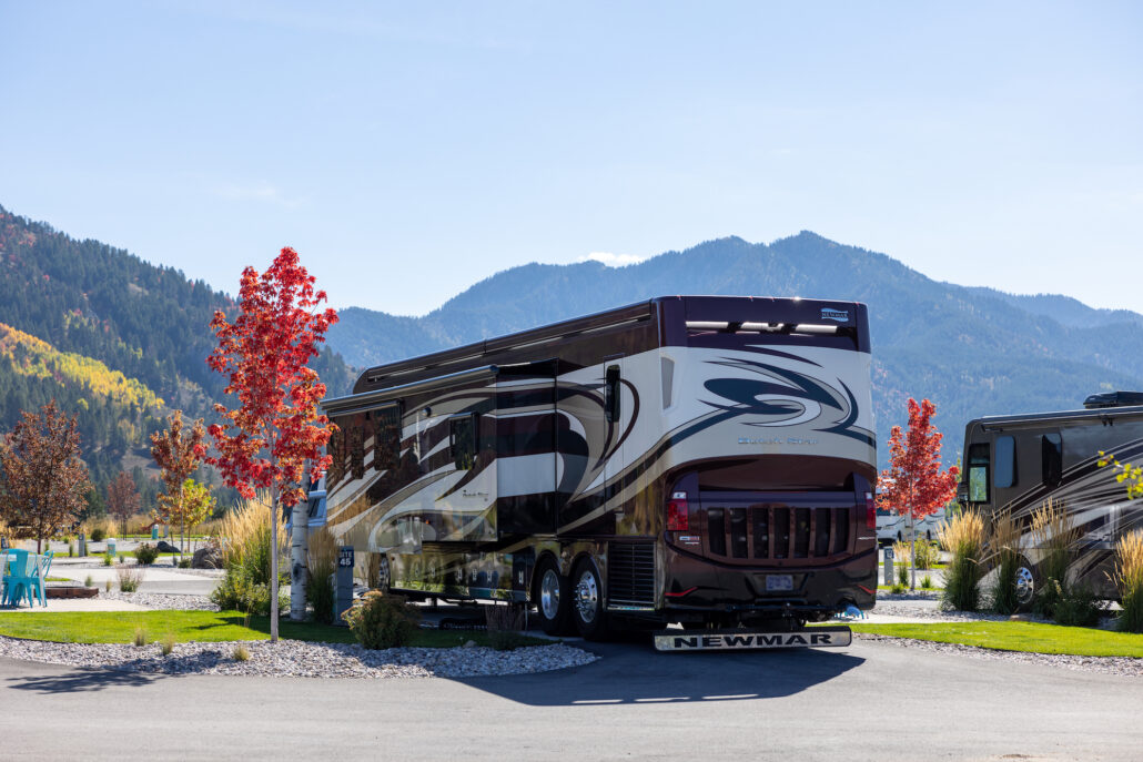 A pull-through RV site with a red tree in the fall.