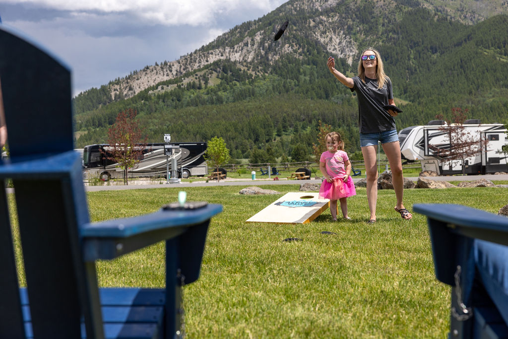 A mother and daughter play lawn games in front of mountains on a sunny day.