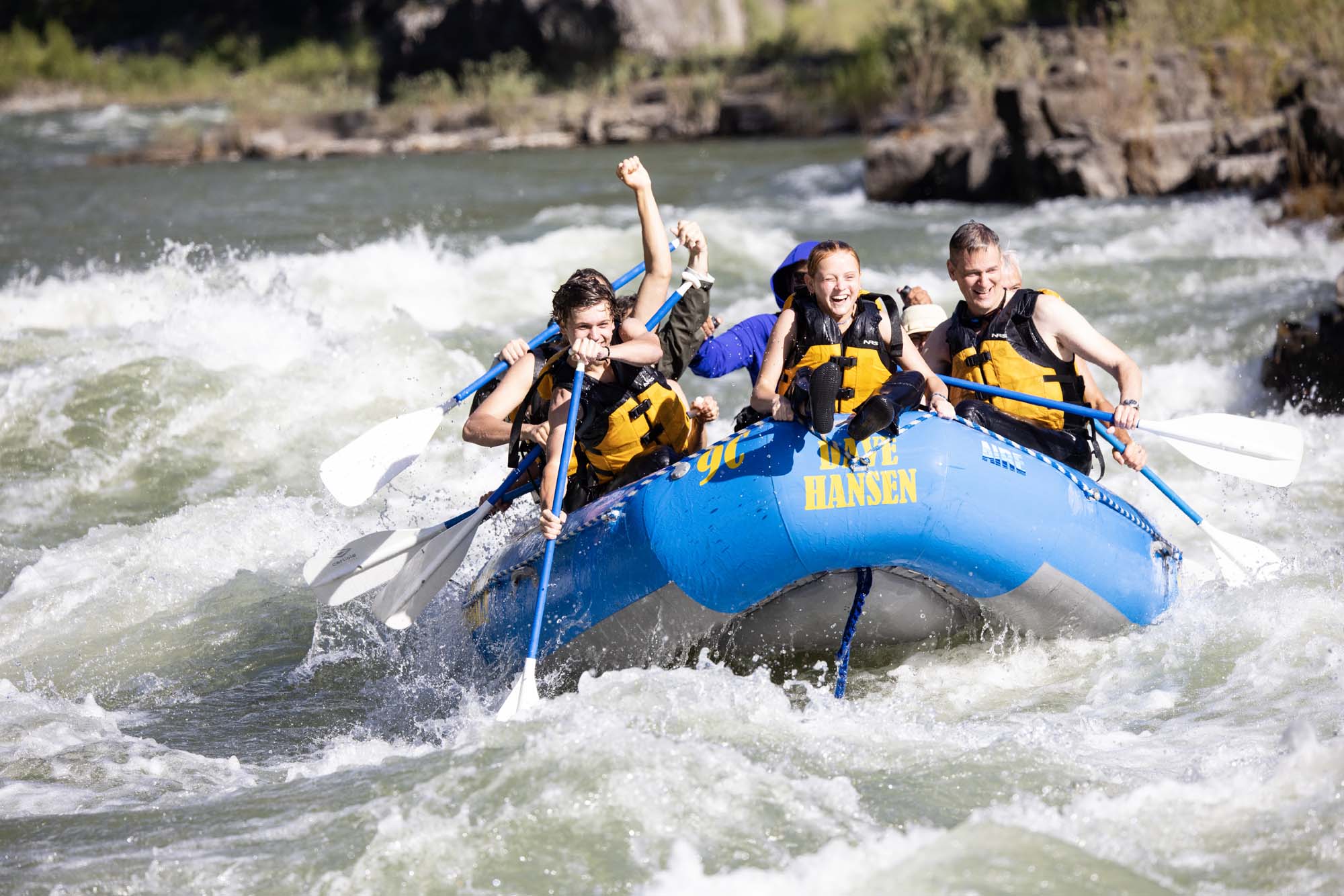A girl smiles in the front of a whitewater raft while charging through a rapid.